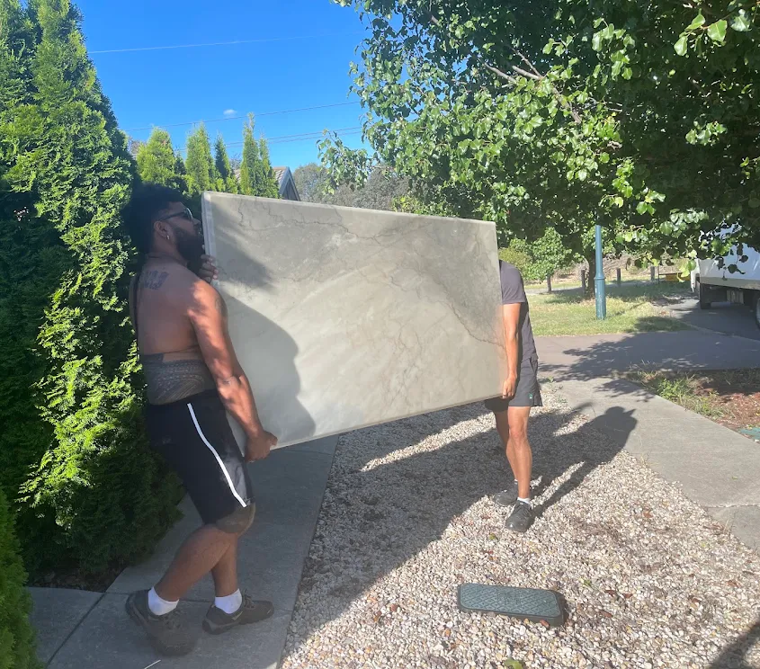 Two Truckmen removalists carrying a large stone piece together